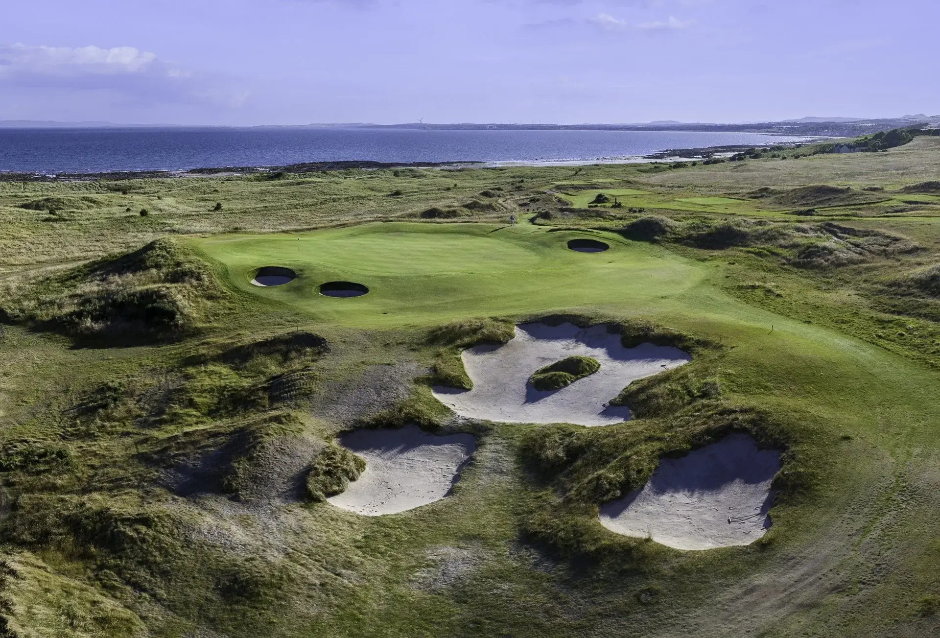 A green and its bunkers at Dumbarnie Links in Fife, set against the Firth of Forth at first light
